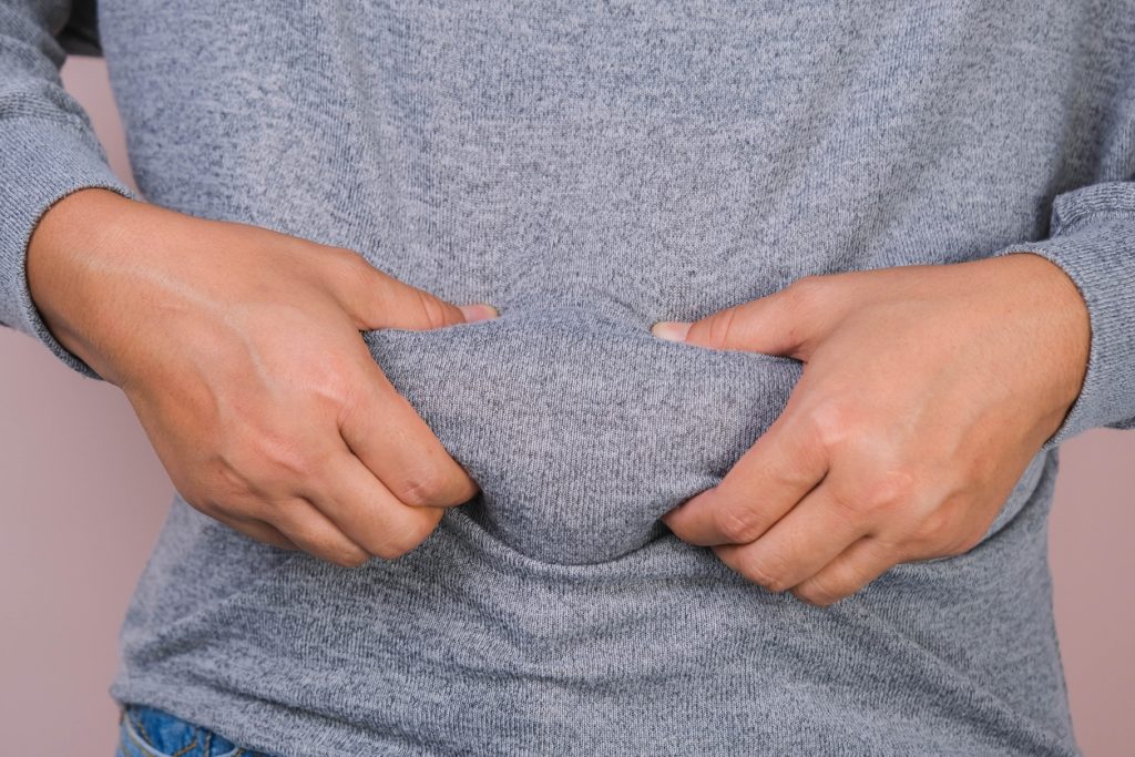 Fat woman hand holding excessive belly fat isolated on pink background. Overweight fatty belly of woman. Female diet and body health care concept