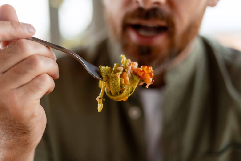 Homme mangeant de délicieuses pâtes au pesto et au saumon